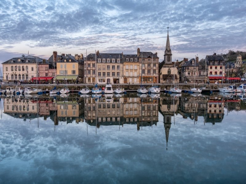 Port de Honfleur avec les bâtiments reflétant sur l'eau sous un ciel nuageux